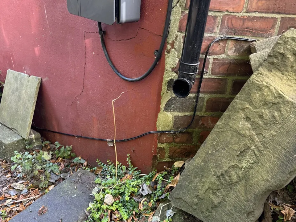 Rainwater downpipe discharging onto open ground at the base of the wall, with no gully