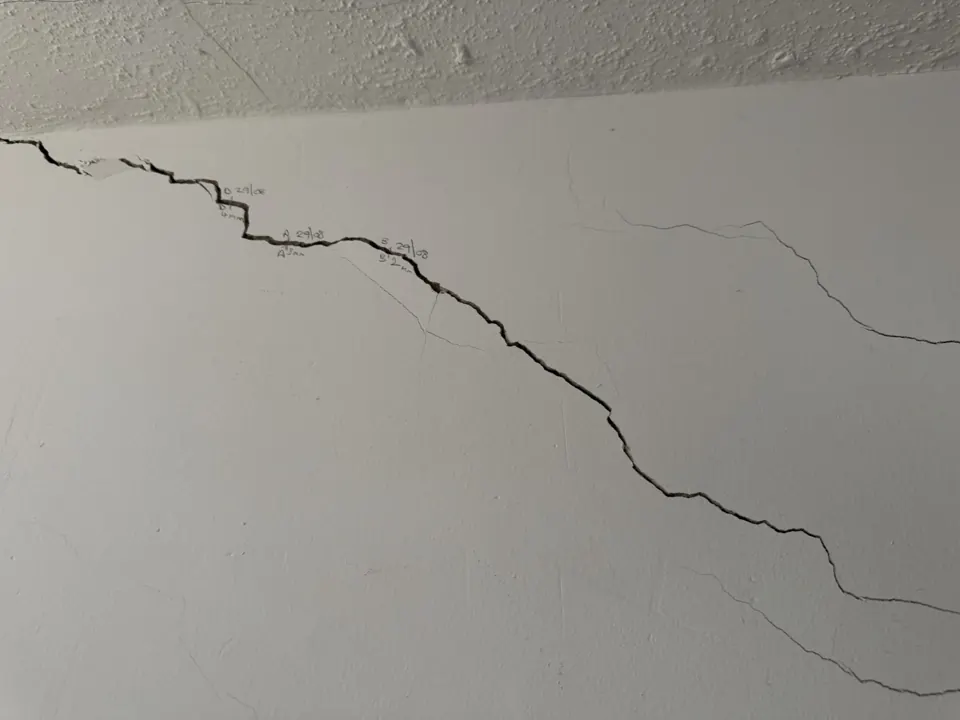 Stepped diagonal crack in a hallway wall rising towards the ceiling, with the owner's pencil reference marks
