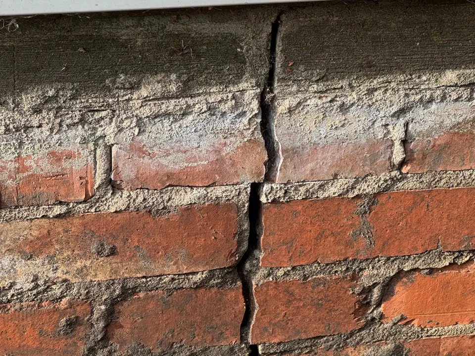 Close-up of an open vertical crack through bricks and mortar below a door sill