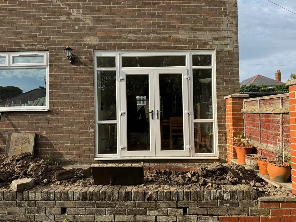 Rear elevation of a brick house with patio doors and the excavated patio in front