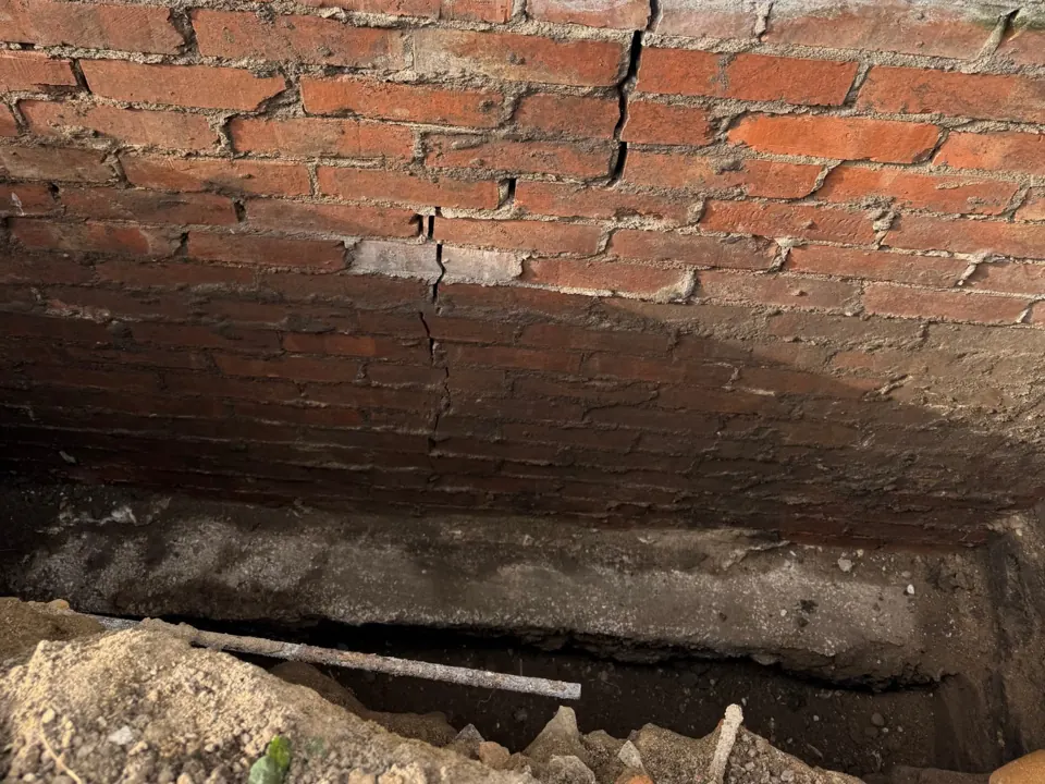 Trial pit exposing brickwork and the concrete foundation, with a vertical crack in the brickwork closing above the foundation